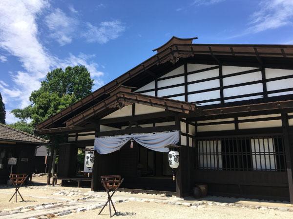 2つの篝火台が建物へと続く通路の両脇にあり、建物の正面入り口には白い幕が上部に掛かってあり、入口両端に白地の提灯が下がっている写真