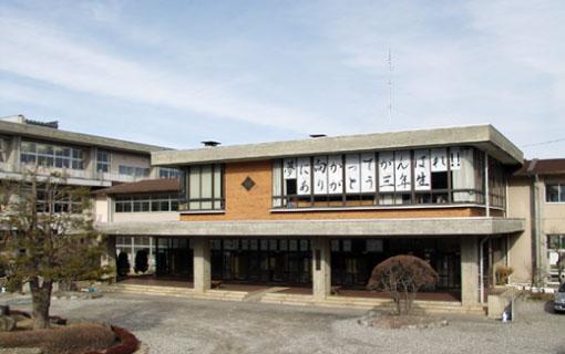 窓に「夢に向かってがんばれ!ありがとう三年生」と書かれた紙が貼ってある、飯島中学校の校舎と植木の写真