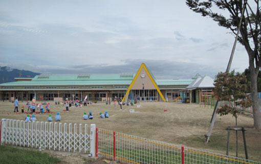 緑色の屋根の飯島東部保育園の園舎と園庭で遊んでいる園児たちの写真