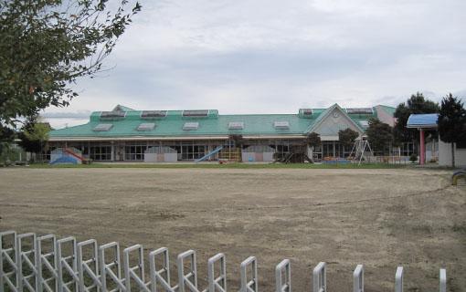 緑色の屋根で平屋づくりの七久保保育園の園舎と広い園庭、滑り台やブランコなどの遊具の写真