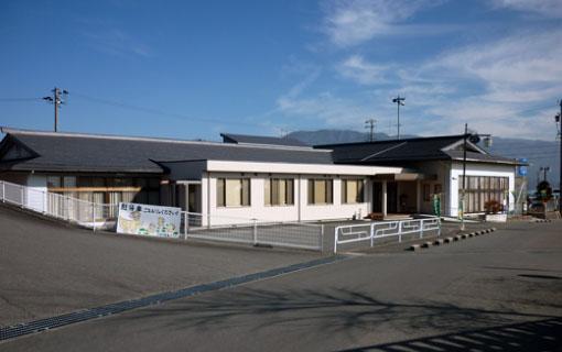 グレー色の屋根に白い外壁で平屋づくりの七久保公民館の建物と建物に面する道路の写真