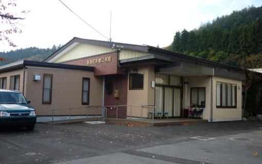 薄い茶色の外壁で平屋づくりの本郷公民館の建物と黒い車の写真