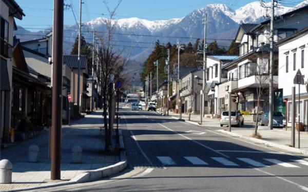 一本の道路を挟んで両側に民家が立ち並び、道路の奥には山々がそびえ立っている写真