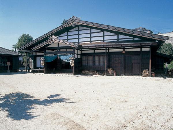 平屋の木造の建物の前に砂が敷かれ、中央の入り口両脇の柱に提灯が下がっている写真
