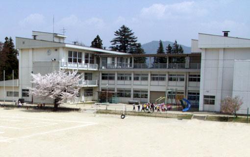 飯島小学校の校舎、運動場、1本の桜の木、遊具と生徒たちの写真