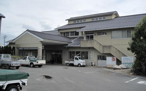 ベージュの外壁の飯島公民館の建物と付近に停めてある4台の車の写真