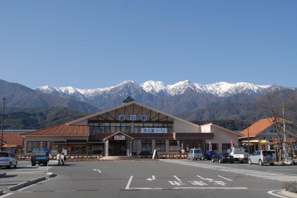 道の駅 花の里いいじまの建物と、背景に頂上が雪に覆われた山脈の写真
