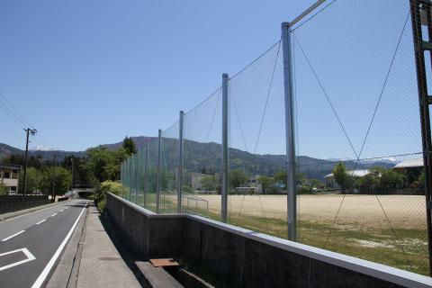 中学校のグラウンドと道路を隔てて建っている防球フェンスの写真